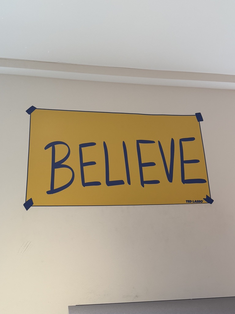 Cartel amarillo «BELIEVE» de Ted Lasso pegado en la pared